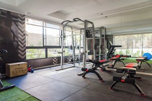 Ein Fitnessstudio mit Gewichthebersportgeräten, Cardiogeräten und einem großen Fenster mit Blick ins Freie.