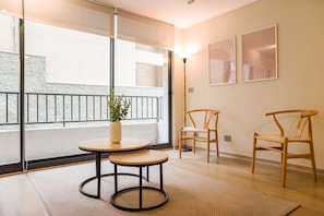 Ein modernes Zimmer mit einem großen Fenster, zwei Holzstühlen, einem kleinen runden Tisch und einer Stehlampe.