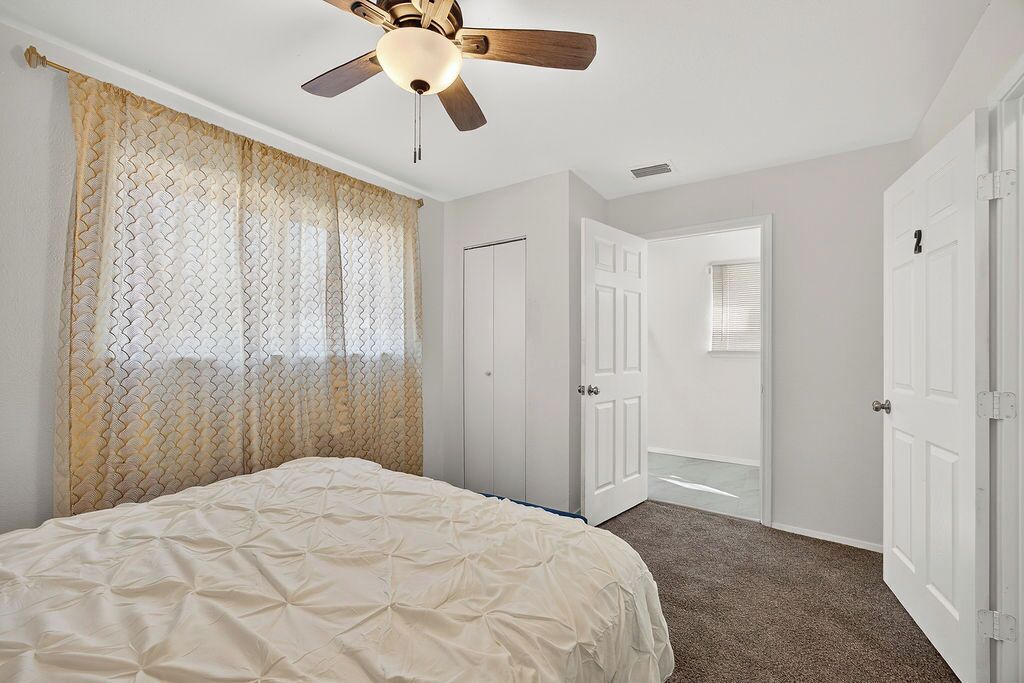 A bedroom with a bed, a ceiling fan, and a door leading to another room.