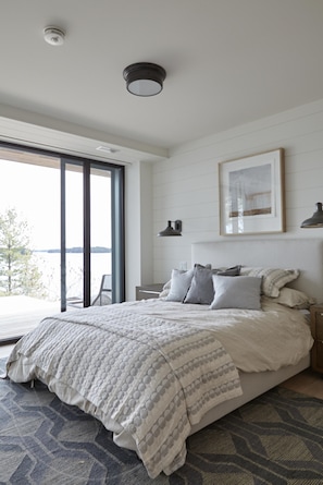 A bedroom with a large bed, a view of the outdoors, and a ceiling light.