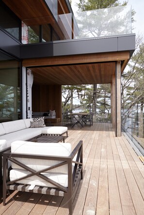 A modern outdoor deck with wooden flooring, a sofa set, and a dining table. - Exquisite 12 bed 13 bath cottage on Lake Joseph (Minett)