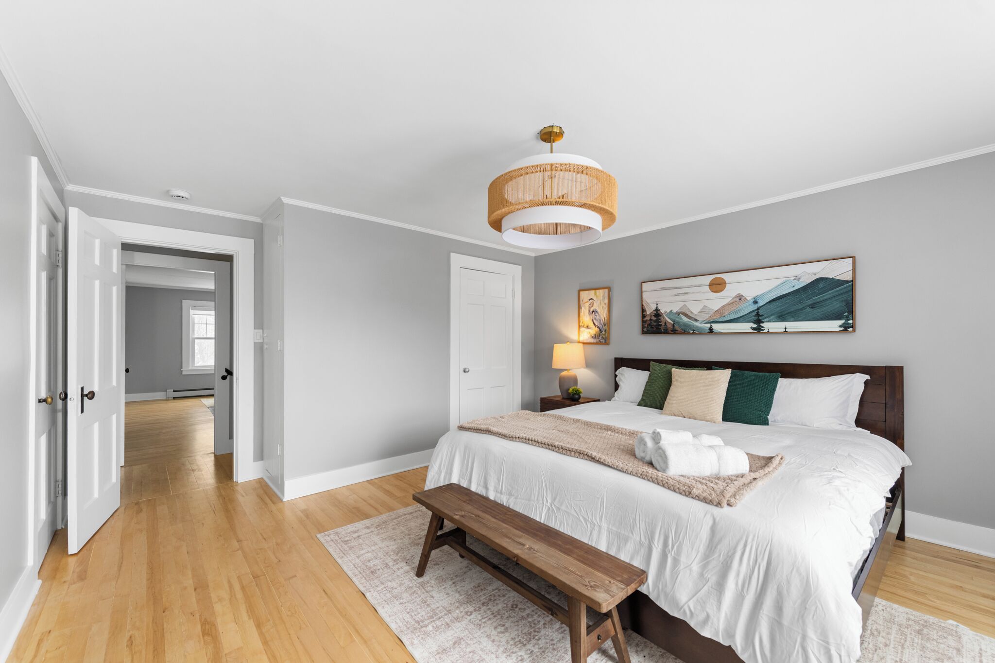 A bedroom with a large bed, a wooden bench, a hanging light fixture, and a painting on the wall.