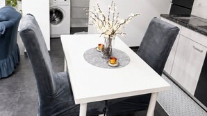 A modern kitchen with built-in appliances, a dining area with a white table and grey chairs, and a grey tiled floor. - Le petit luxe urbain (Bussigny)