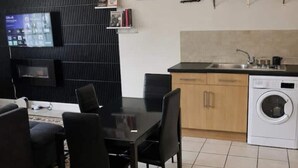 Un espace de vie compact comprenant un coin repas, une cuisine avec machine à laver et un meuble de rangement noir intégrant un téléviseur à écran plat.
