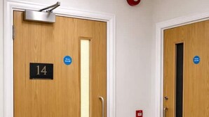 Un couloir avec deux portes en bois, chacune portant une plaque avec un numéro et un panneau bleu.