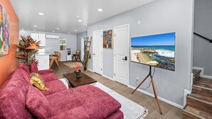 A living room with a large beach painting, a red sofa, and a wooden coffee table. - Boho Vibrant San Diego House w/Patio, Grill & Games (San Diego)