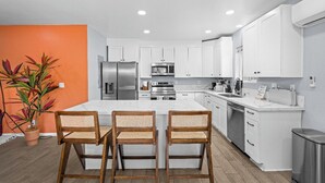 A modern kitchen with white cabinets, a stainless steel refrigerator, and a large island with bar stools. - Boho Vibrant San Diego House w/Patio, Grill & Games (San Diego)