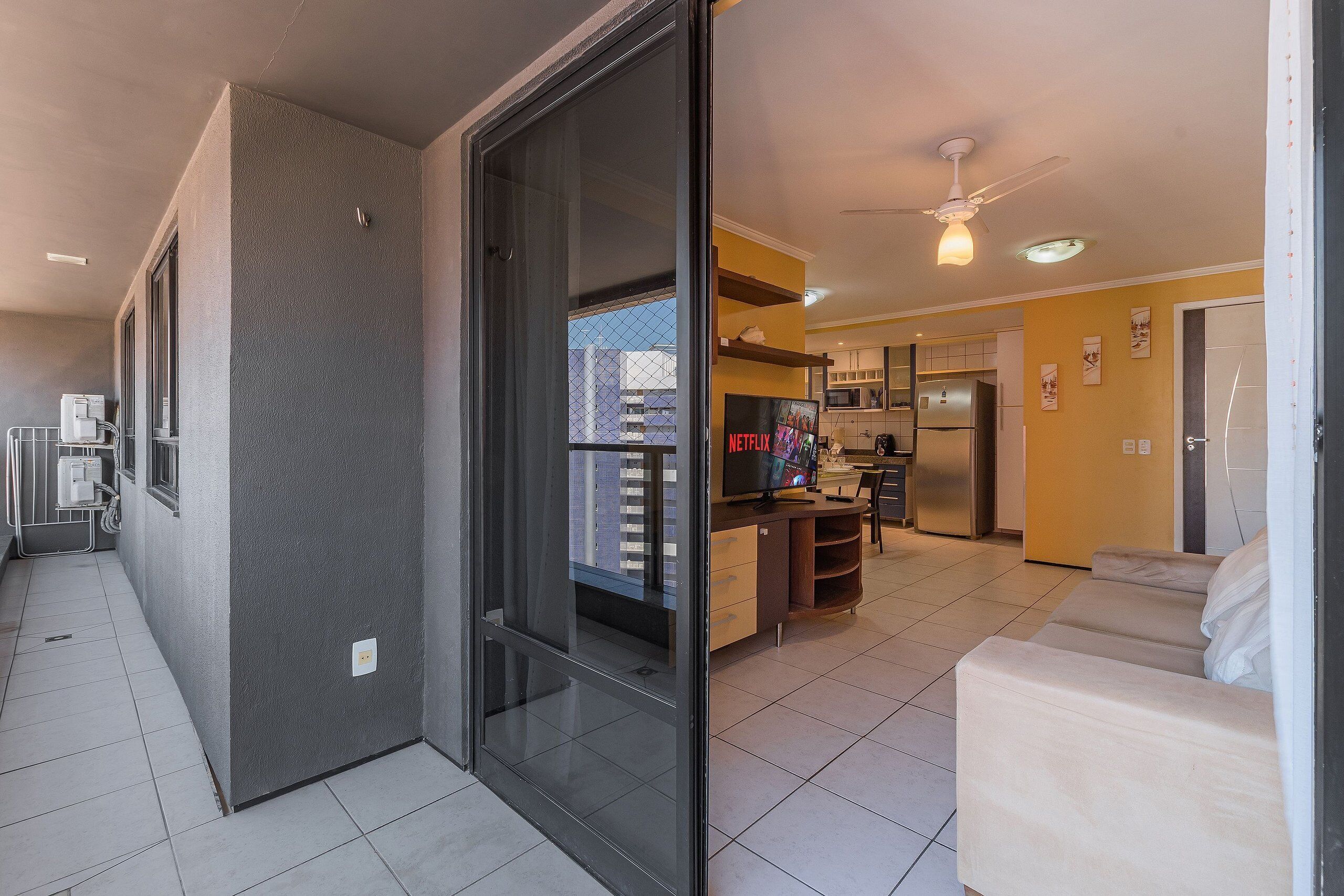 Un appartement moderne doté d’une porte-fenêtre coulissante donnant sur un balcon, d’une kitchenette, d’un espace de vie avec un canapé et d’un ventilateur de plafond.