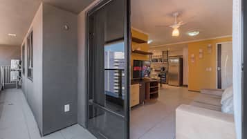 Un appartement moderne doté d’une porte-fenêtre coulissante donnant sur un balcon, d’une kitchenette, d’un espace de vie avec un canapé et d’un ventilateur de plafond.