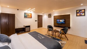 Quarto de hotel moderno com cama, escrivaninha, televisão e área de estar.
