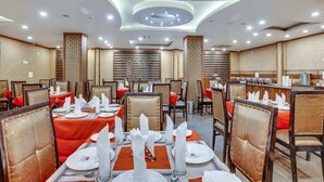 Restaurante com várias mesas dispostas, com toalhas brancas e guardanapos vermelhos, design de teto moderno e painéis de madeira nas paredes.
