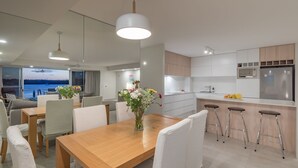 Una cocina moderna con una isla central, taburetes de bar y una zona de comedor con mesa y sillas de madera.