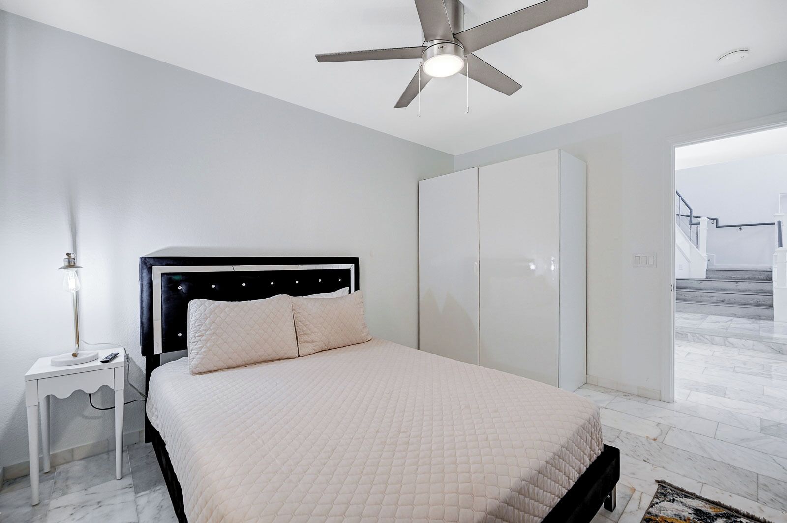 Un dormitorio con cama, mesita de noche, ventilador de techo y armario.