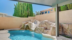 A swimming pool with a waterfall feature, surrounded by stone walls and a covered area.