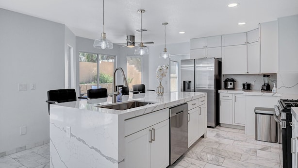A modern kitchen with a large island, stainless steel appliances, and pendant lighting.