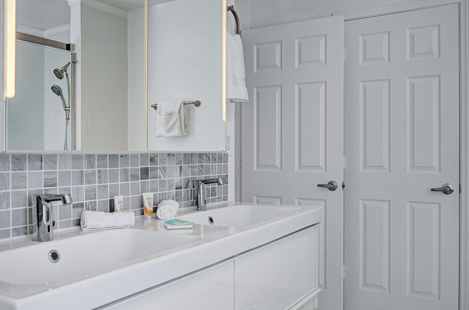 A modern bathroom with a double sink, a mirror, and a shower.