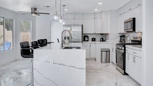 A modern kitchen with white cabinets, a marble countertop, a built-in oven, and a ceiling fan.