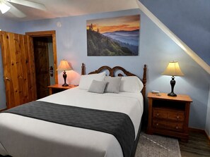 Une chambre à coucher avec un lit, deux tables de chevet, une armoire en bois et un tableau accroché au mur.