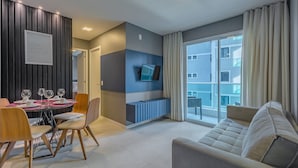 Ett modernt vardagsrum med en soffa, ett matbord och stolar. Det finns en tv monterad på väggen och ett fönster med gardiner.