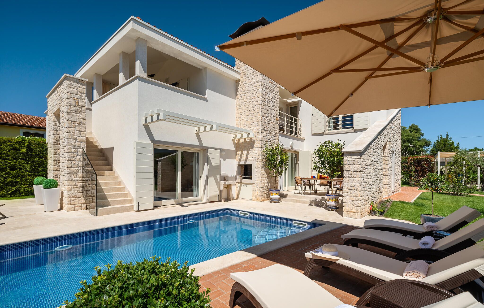 A modern two-story house with a swimming pool, outdoor seating, and a stone facade.