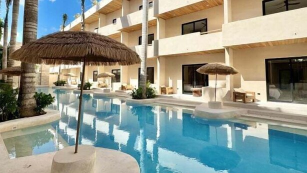 Un hôtel à plusieurs étages doté d’une piscine, d’un espace extérieur aménagé et de palmiers.