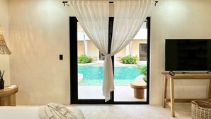 Une chambre avec un lit, une télévision, une petite table et une vue sur une piscine extérieure.
