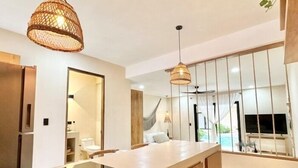 Une cuisine moderne dotée d’un îlot central, de luminaires suspendus et offrant une vue sur une piscine et un espace extérieur.