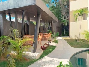 Uma área de estar moderna ao ar livre, com piscina, rodeada por vegetação e palmeiras.