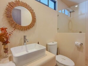 Um banheiro com pia branca, vaso sanitário e espelho com moldura em forma de raios de sol.