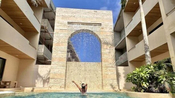 Un área de piscina con una piscina azul cristalina, un arco de piedra y una persona de pie en el agua.