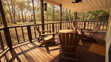 Um deck de madeira com cadeiras Adirondack, uma mesa e um candeeiro.