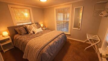 Quarto com cama, luminárias de cabeceira, espelho e janela com persianas.