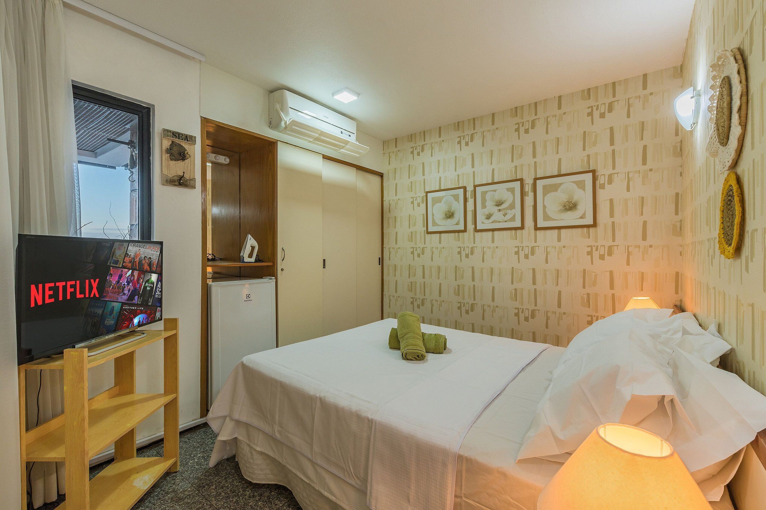 Habitació d'hotel amb un llit, un televisor sobre un suport de fusta, aire condicionat fixat a la paret i una porta que dona a un bany.