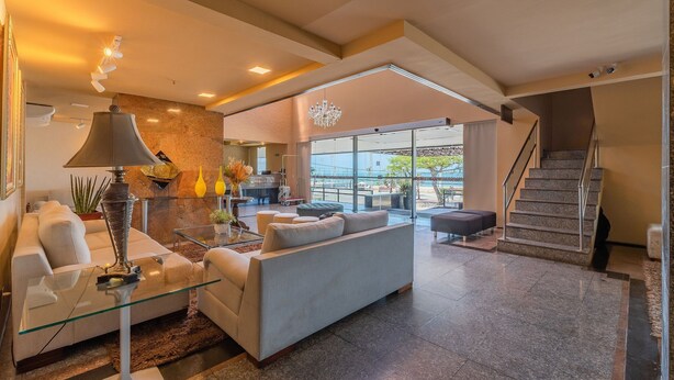 A spacious living area with a modern sofa, a glass coffee table, and a lamp. A staircase is visible in the background leading to an upper level. - Iracema Residence #103 - Seafront by Carpediem (Fortaleza)