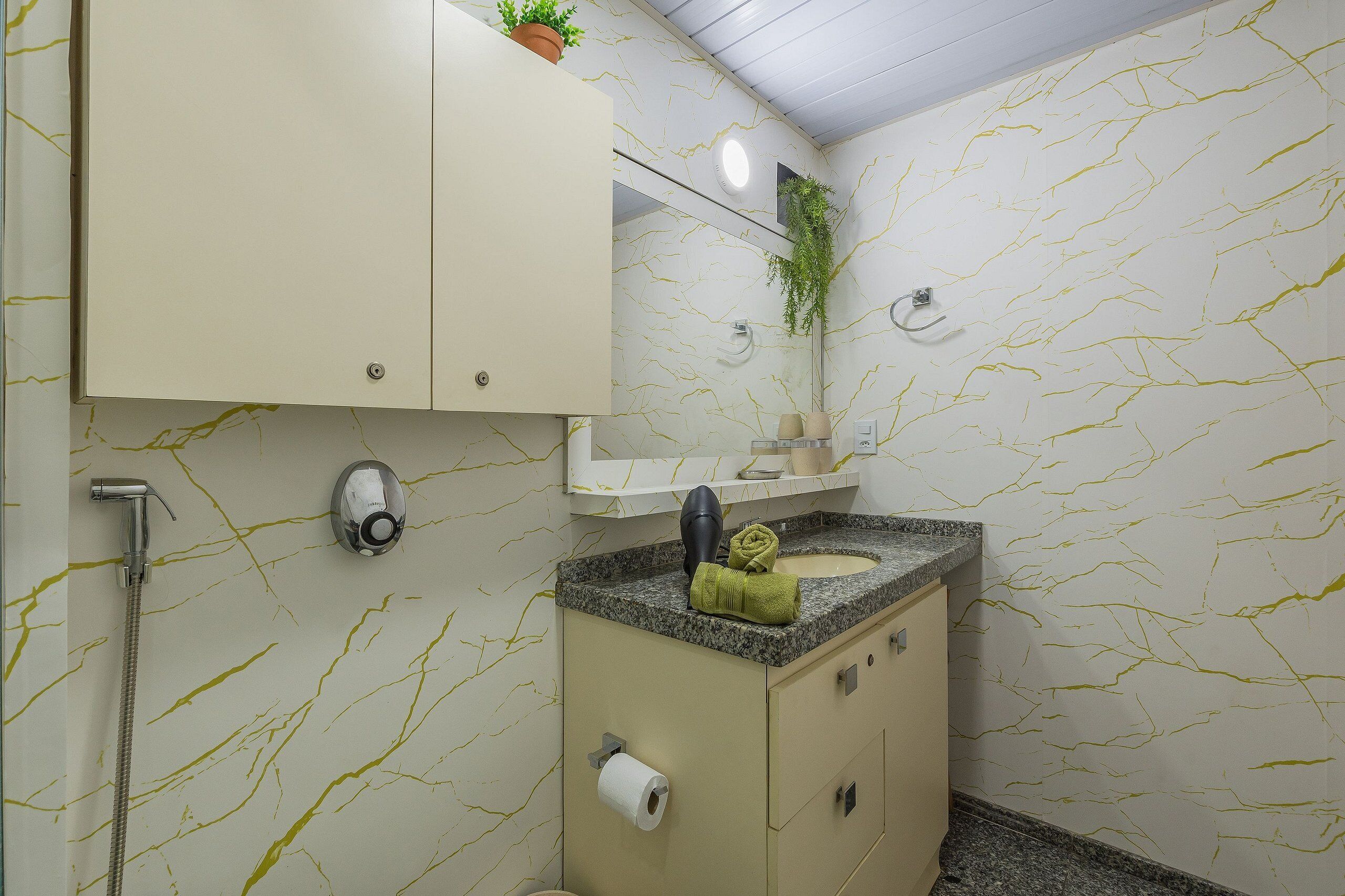 Casa de banho com parede com padrão marmorizado, pia com bancada de granito, toalha e suporte para papel higiénico.