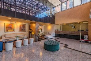 A hotel lobby with a high ceiling, a reception desk, seating area with couches and ottomans, and artwork on the walls. - Iracema Residence #103 - Seafront by Carpediem (Fortaleza)