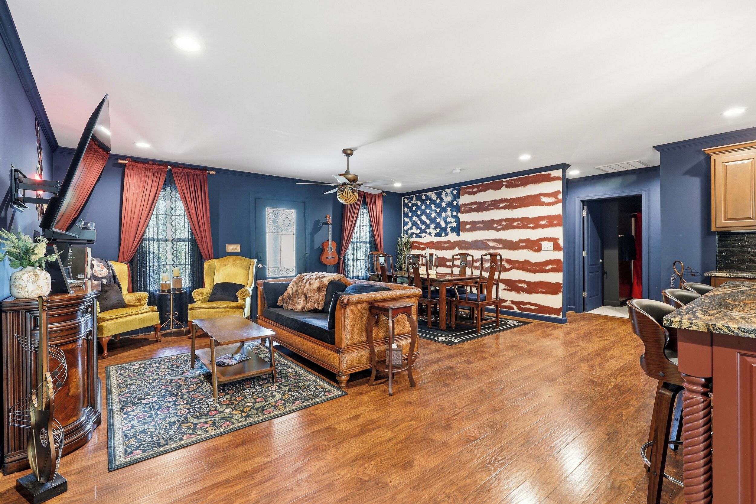 A spacious living room with a sofa, chairs, a dining table, and a large American flag mural.