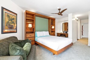 Ein Schlafzimmer mit einem hölzernen Bett, einem Nachttisch, einer Kommode, einem Deckenventilator und einem gerahmten Bild an der Wand.