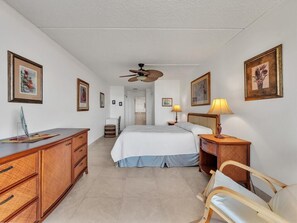 Ein Hotelzimmer mit Bett, Nachttisch, Lampe, Holzkommode und Deckenventilator.