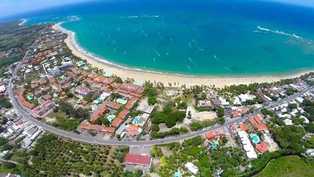 Una vista aerea di una zona costiera con una spiaggia, edifici residenziali e una strada.