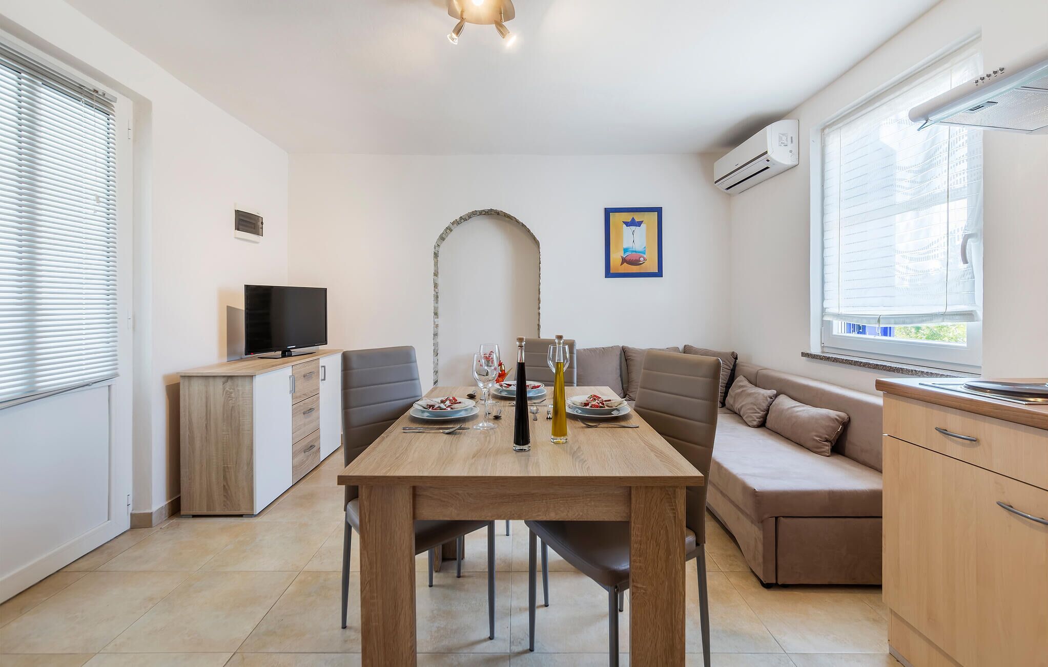 Une cuisine moderne avec un coin repas, comprenant une table en bois, un four encastré et un téléviseur.