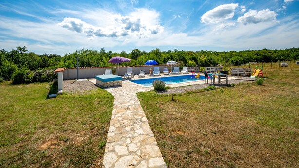 A backyard with a swimming pool, stone pathway, and outdoor seating area with umbrellas. - Lovely apartment in Trget (Trget)