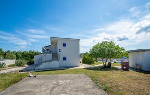 A modern, single-story building with a flat roof, a small balcony, and a concrete pathway leading to the entrance. - Lovely apartment in Trget (Trget)