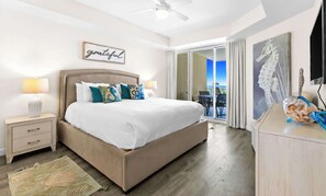 A bedroom with a bed, bedside tables, a ceiling fan, a view to the outside, and a painting on the wall. - The Crescent 215 (Destin)
