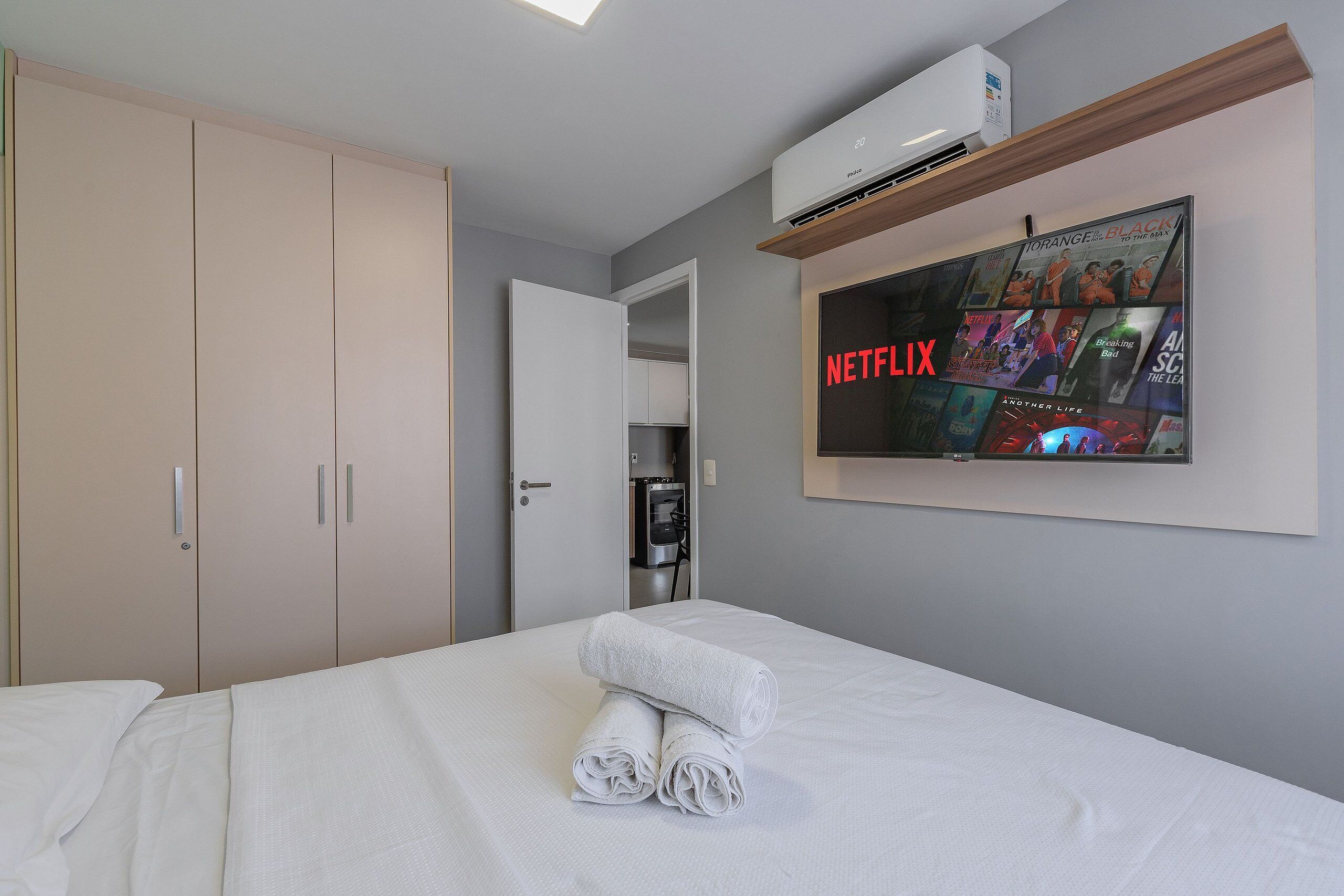 A hotel room with a bed, a wall-mounted TV displaying Netflix content, and a water dispenser.