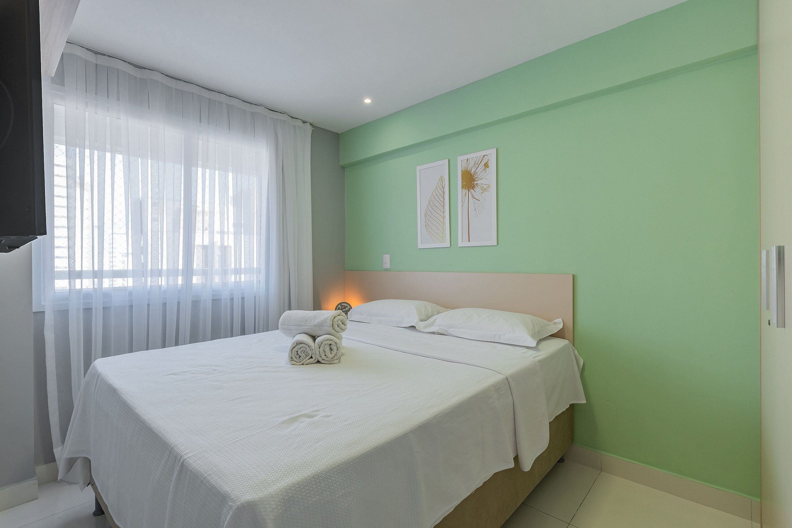 A neatly made bed with white linens and rolled towels, a bedside table, and two framed pictures on the wall.