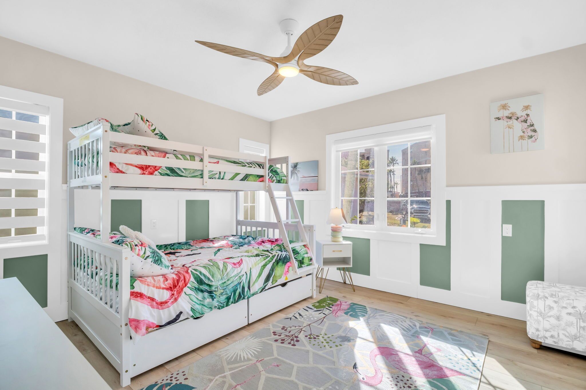 A child’s bedroom with bunk beds, a ceiling fan, a desk, and a window with a view.