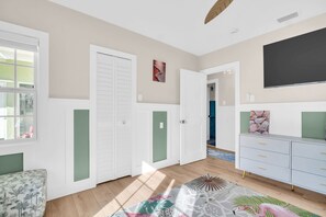 A room with a bed, a dresser, a television, and a door leading to another room. - Coastal Bungalow Steps from Redington Beach, Walk to Dining & Sunsets (North Redington Beach)
