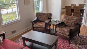 Una sala de estar con un sofá rojo, sillones estampados, una mesa de centro de madera y una zona de comedor con sillas de mimbre.