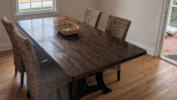 Un comedor con una mesa de madera oscura, sillas de mimbre y una cesta sobre la mesa.